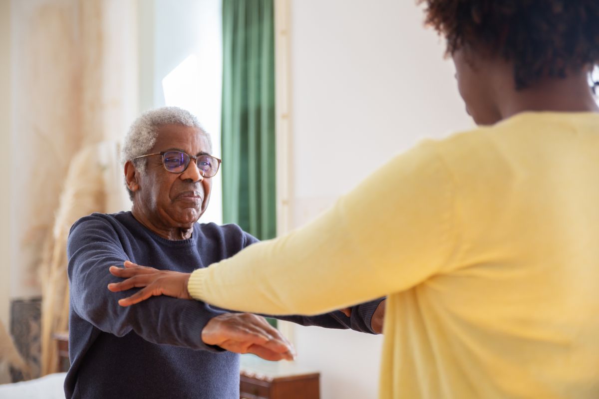 An older man practicing an arm exercise with individual guidance